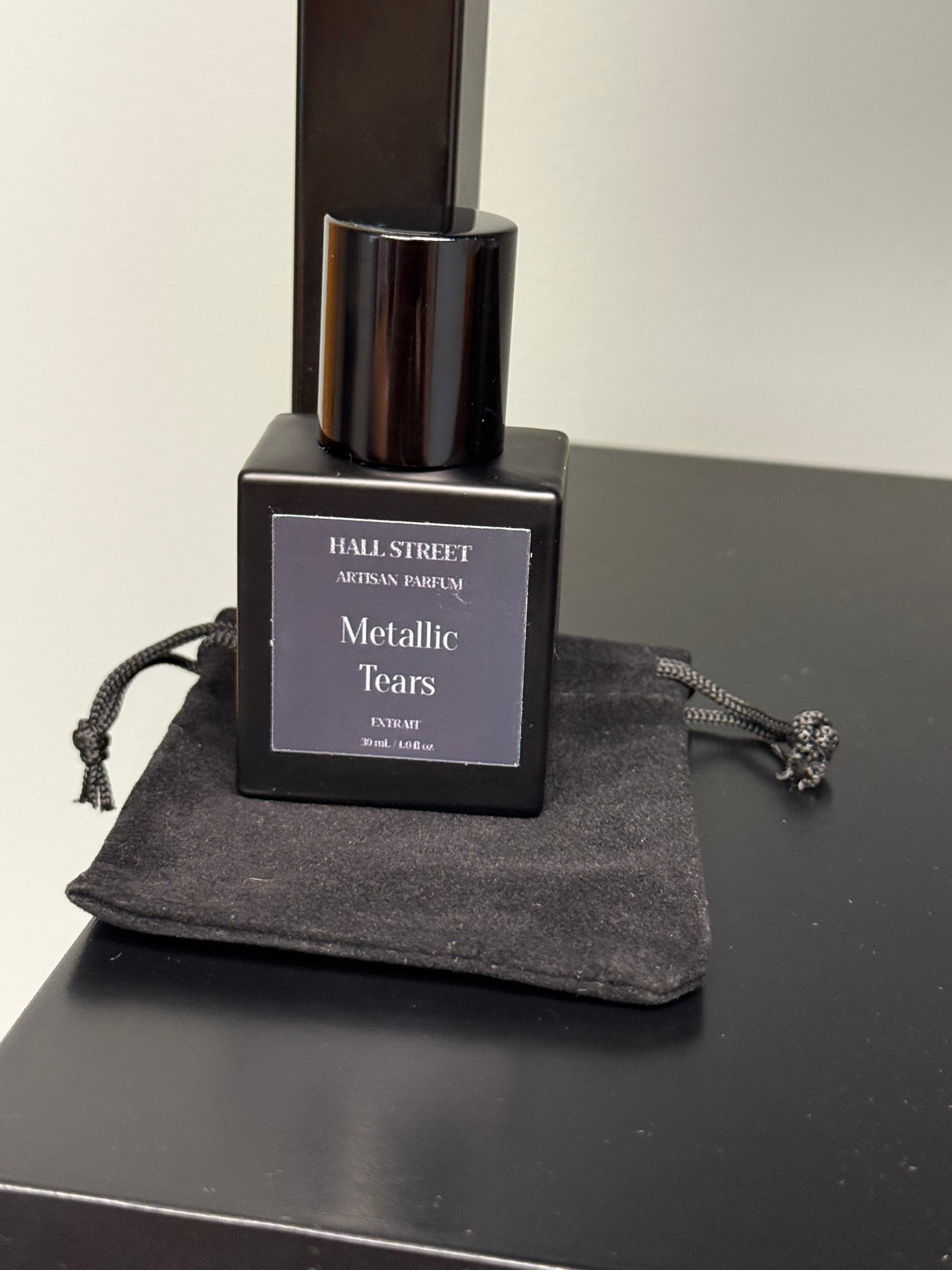Black perfume bottle labeled  Metallic Tears by Hall Street Artisan Parfum on a dark surface.
