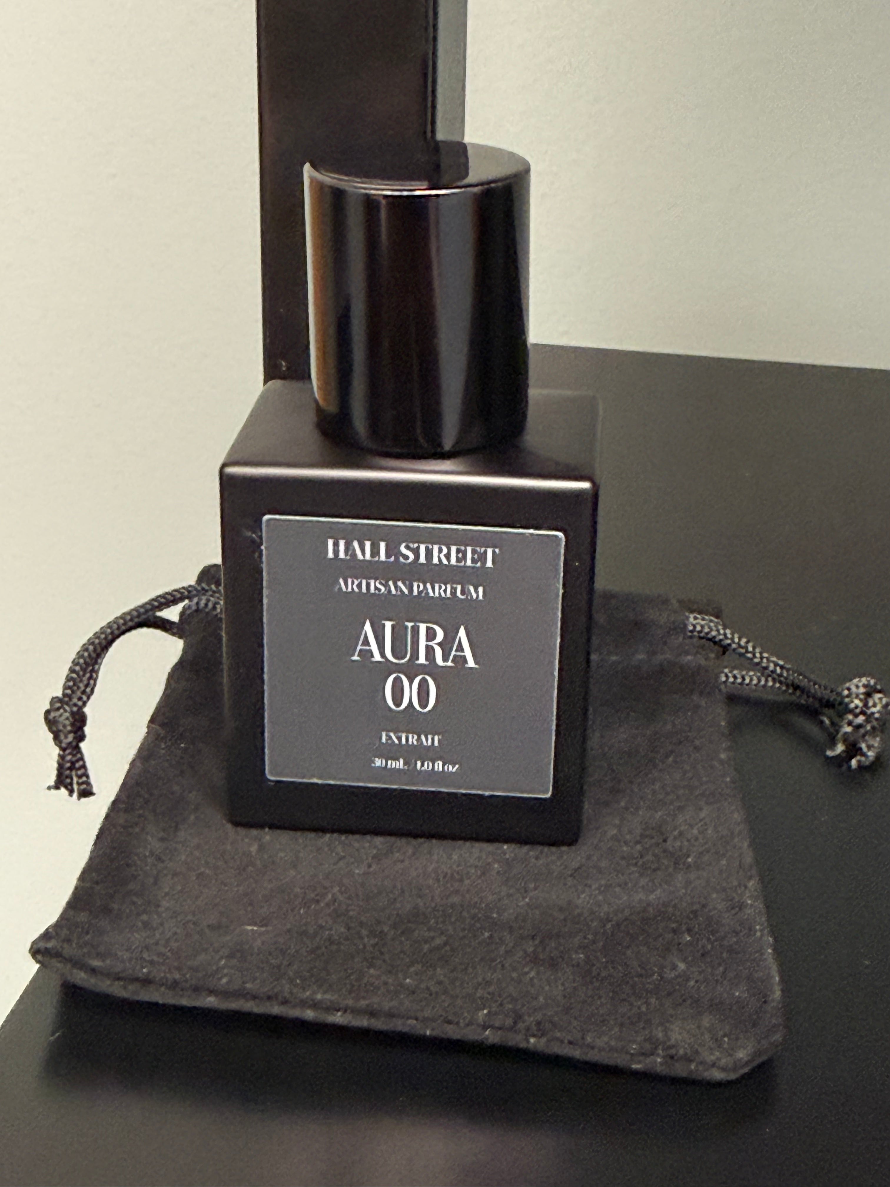 Black perfume bottle labeled  Aura00 by Hall Street  Artisan Parfum on a dark surface.