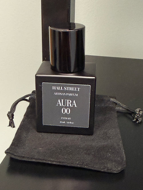 Black perfume bottle labeled  Aura00 by Hall Street  Artisan Parfum on a dark surface.