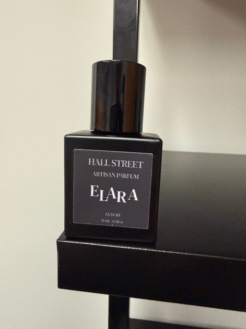 Black perfume bottle labeled ELARA by Hall Street Artisan Parfum on a black surface with a neutral background.